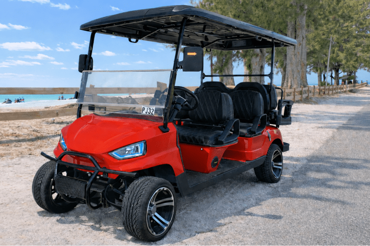 Red golf cart on a beachside road with trees and ocean in the background.