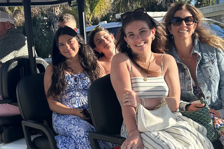 Group of five people smiling on a golf cart in sunny weather.