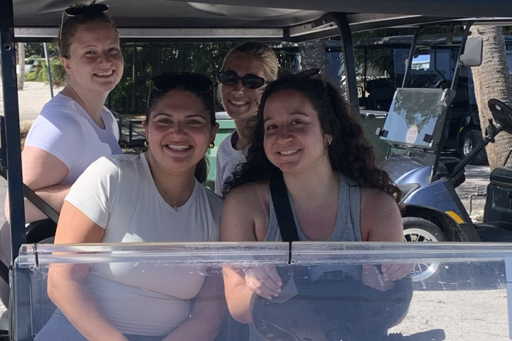 Four people smiling inside a golf cart near palm trees.