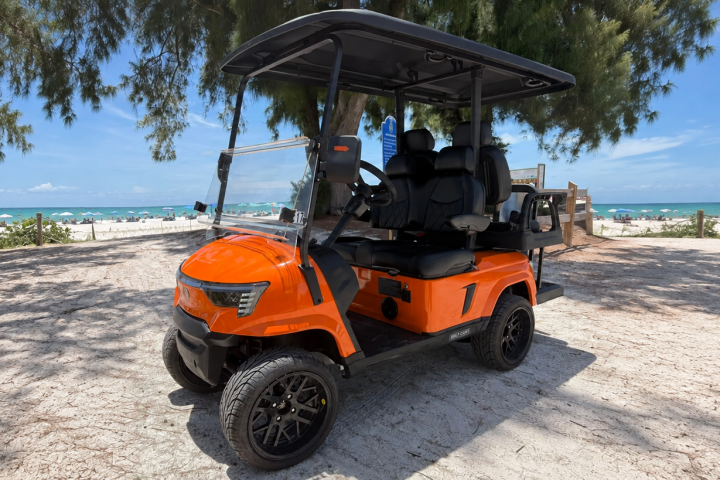 Orange golf cart parked on a sandy beach path with ocean view.
