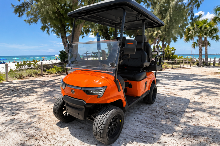 Orange golf cart on sandy path near a beach with palm trees.
