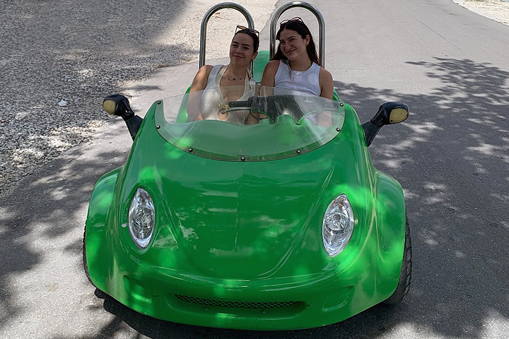 Two people smiling in a green dune buggy on a sunny road.