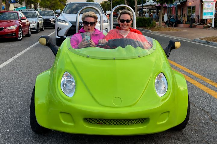 Two people in a bright green, open-top car on a street, wearing colorful clothes.