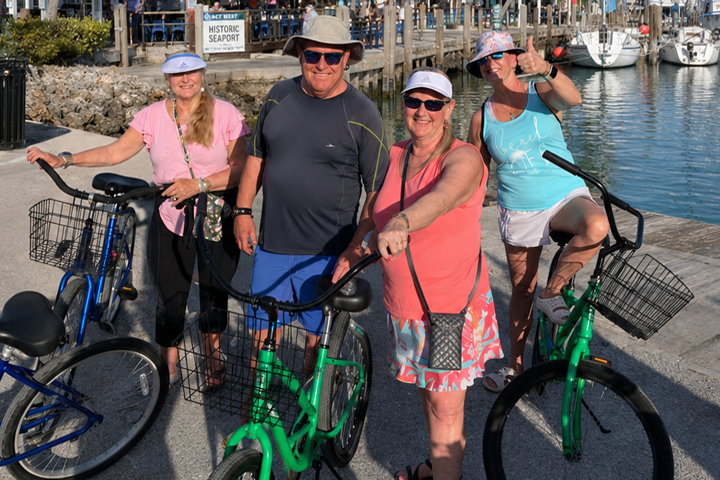 Four people standing with bicycles at a marina, smiling in sunny weather.