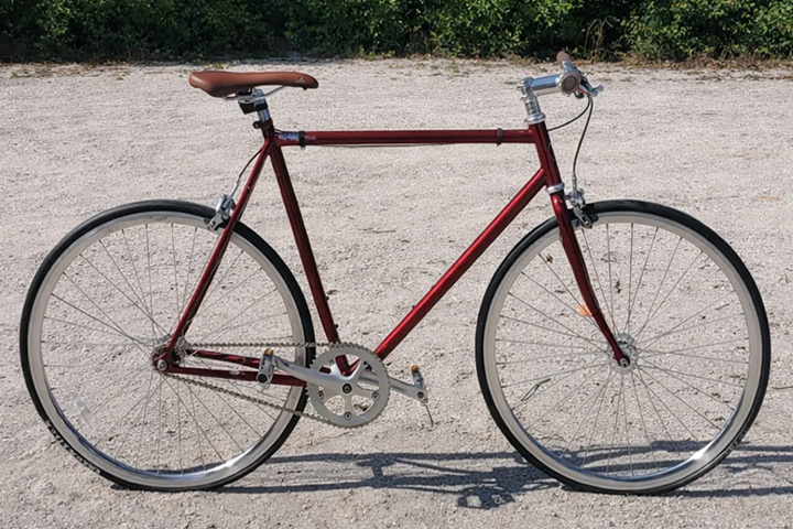 Red vintage bicycle with brown seat on gravel path.