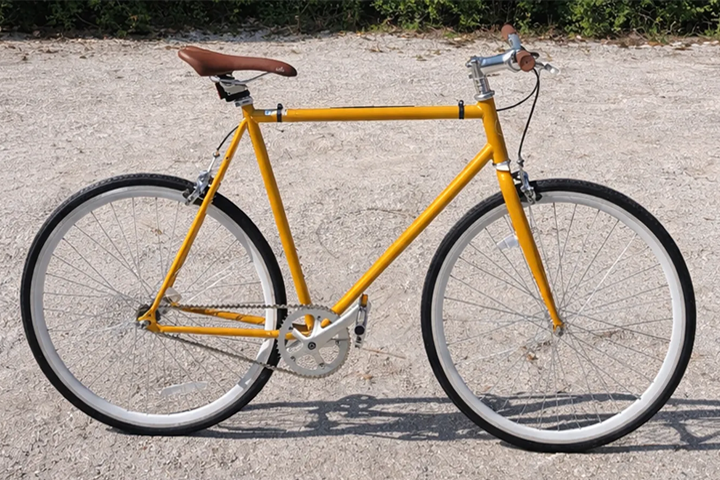 Yellow bike with brown saddle on gravel path.